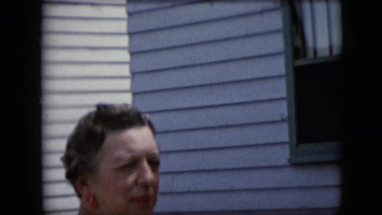 Woman looking to the side outside a light-sided house.