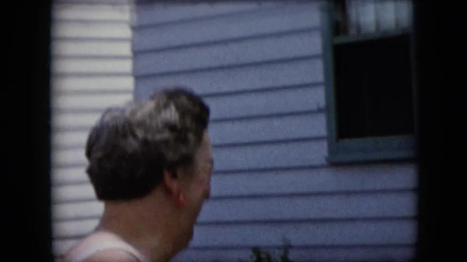 The woman is shown from behind near the same pale-sided house, with her short hair, red earring, window trim, and another partial figure low in frame visible.
