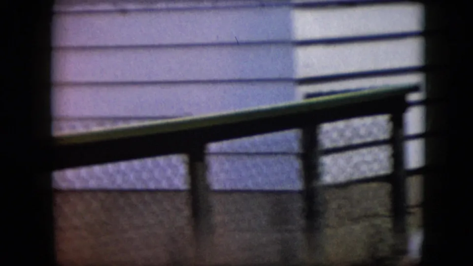 1969 California home-movie frame with suburban house siding, fence, and railings visible while the gathering is largely outside the frame.