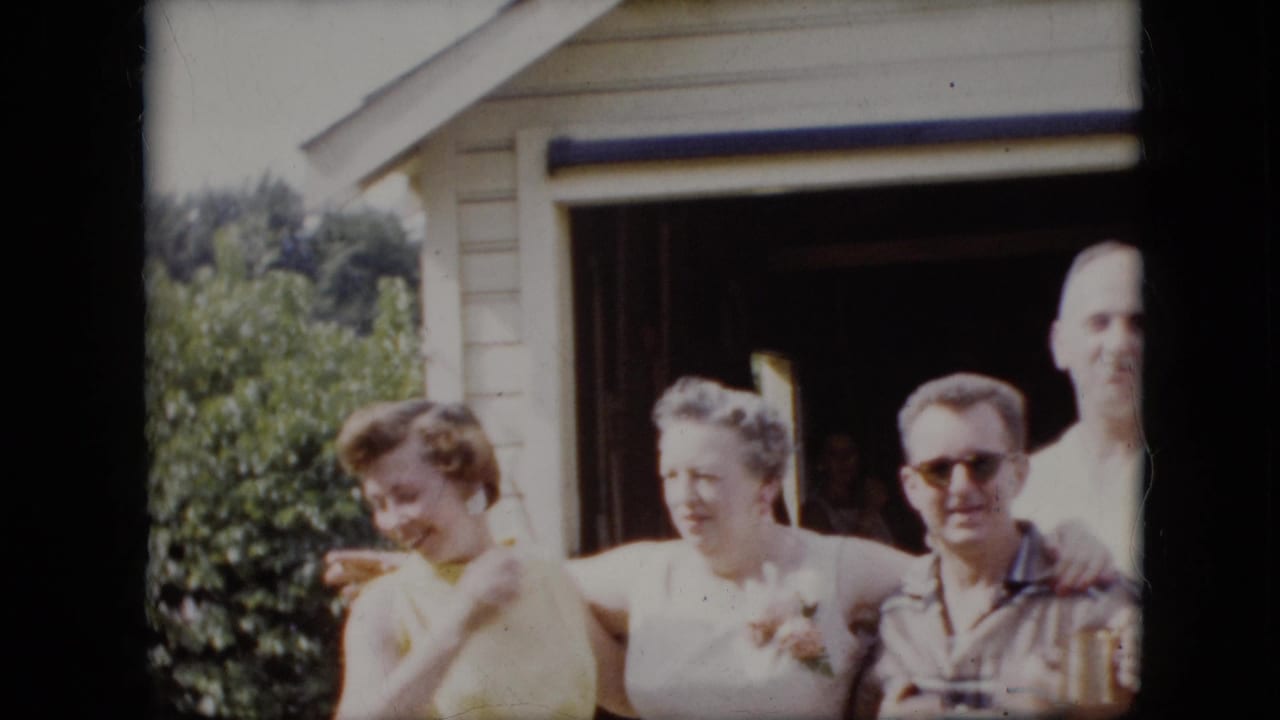 Four adults stand close together outside an open garage, with one woman in yellow looking aside.