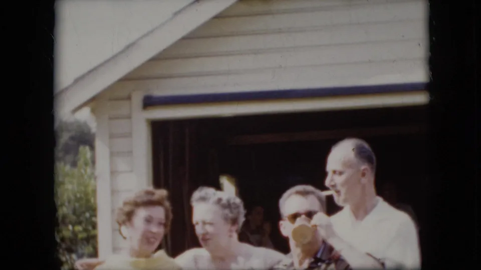 Near the end of the 1969 California shot, the adult group remains in front of the open garage while the man in sunglasses drinks and the taller man smokes nearby.