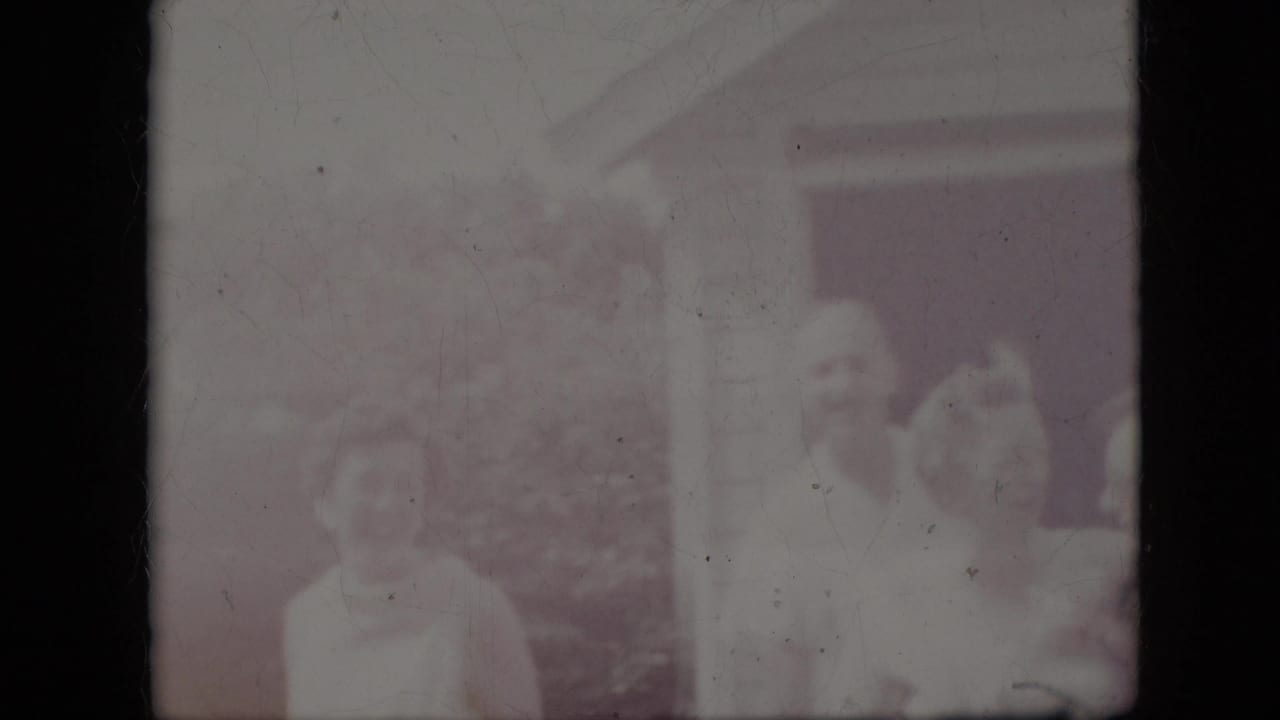 Faded frame of adults near a house exterior, with figures barely visible.