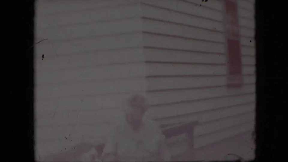 Soft, faded 1969 California home-movie frame showing exterior siding or porch detail, with a faint partial figure near the lower edge and visible film grain and discoloration.