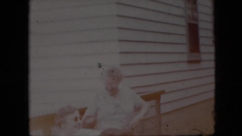 Faded 1969 California 8mm frame showing a house exterior with horizontal siding, a porch railing, and an overexposed indistinct figure near the lower left.