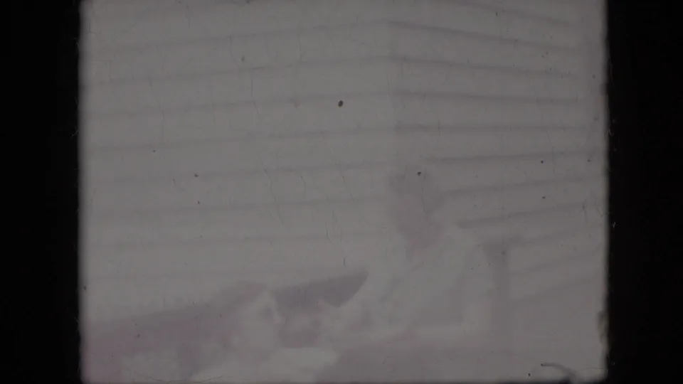 Washed-out 1969 California 8mm frame with faint horizontal siding, pale indistinct forms, film dirt, and heavy exposure loss obscuring the scene.