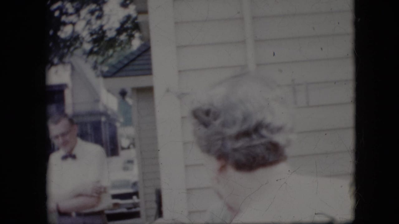 Man in a bow tie stands near adults outside a light-sided house.