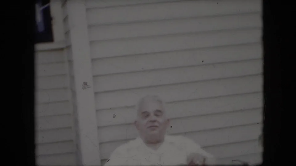 The final visible frame shows the elderly man outside the light-sided house, his expression more neutral as he looks near the camera in soft daylight.