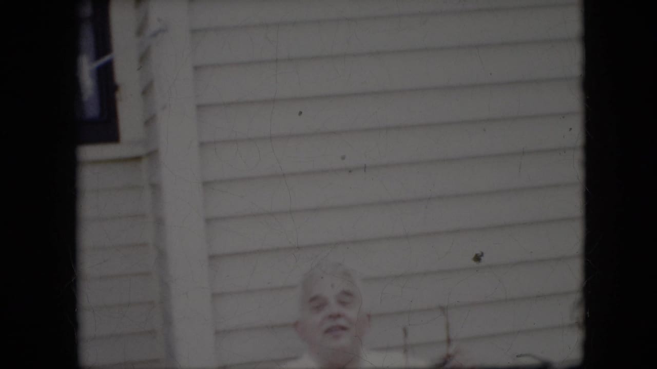 White-haired elderly man partly visible in front of a light-sided house.