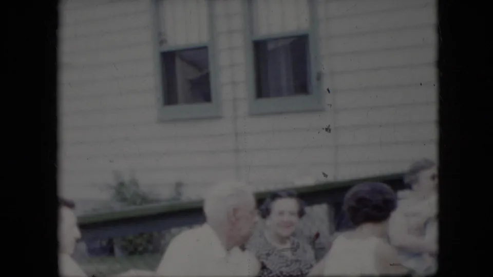 A small group of adults stands outside the California residence, with an older white-haired man turned toward women near the house windows.