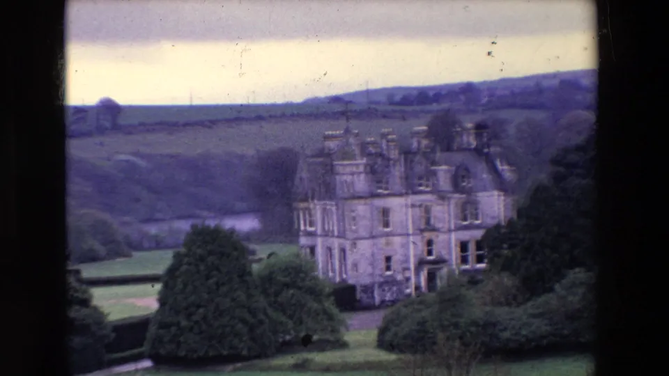 The 1969 Ireland home-movie view settles on a stone castle with landscaped greenery, fields, and low hills beyond.