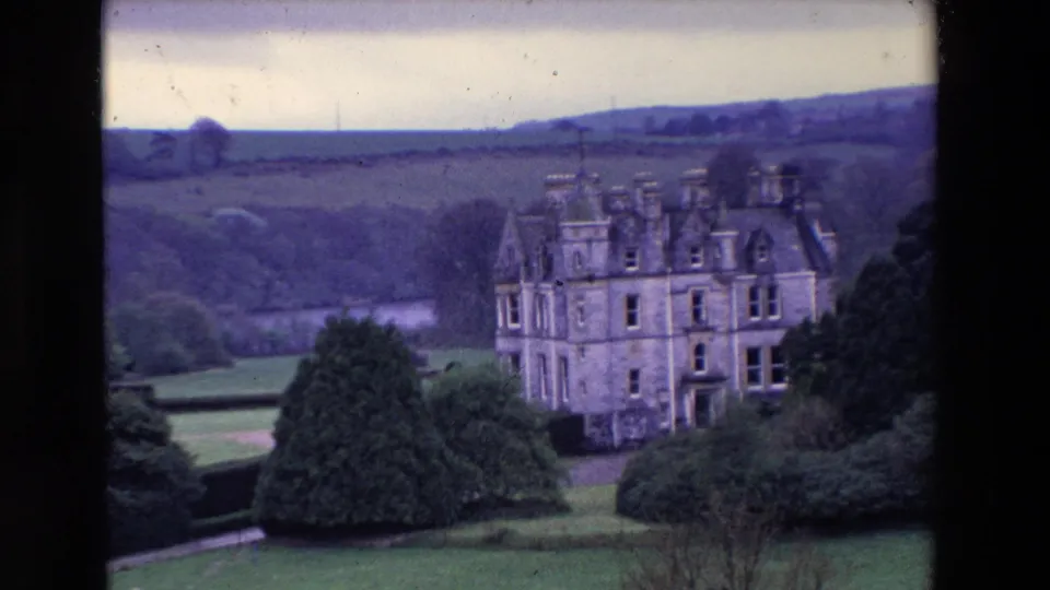 Final 8mm frame of the Ireland clip showing the turreted stone estate building near the right side of the frame, with gardens, trees, and rolling hills behind.