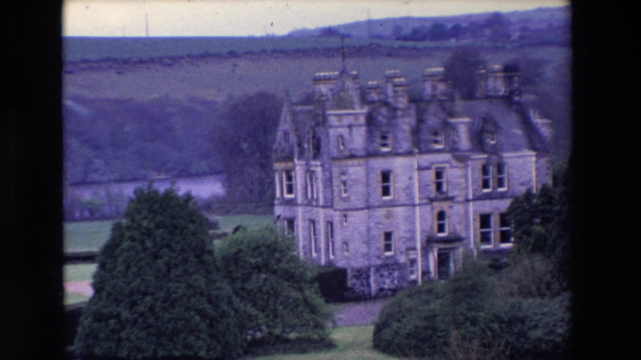 Wide view of a large stone castle set among trees, hedges, lawns, and distant hills.