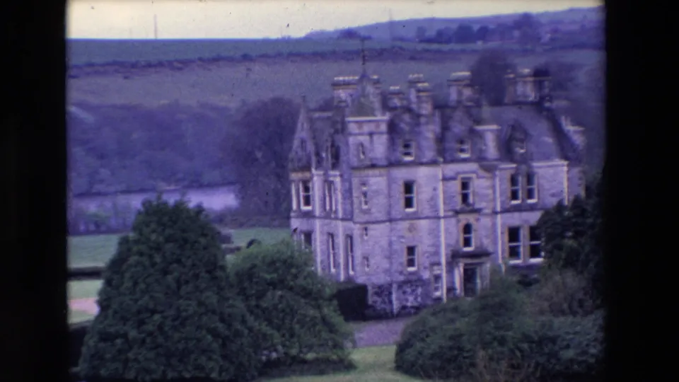 Wide 1969 Ireland home-movie view of a large historic stone castle in green countryside, with trees, hedges, lawns, and rolling hills visible beyond.