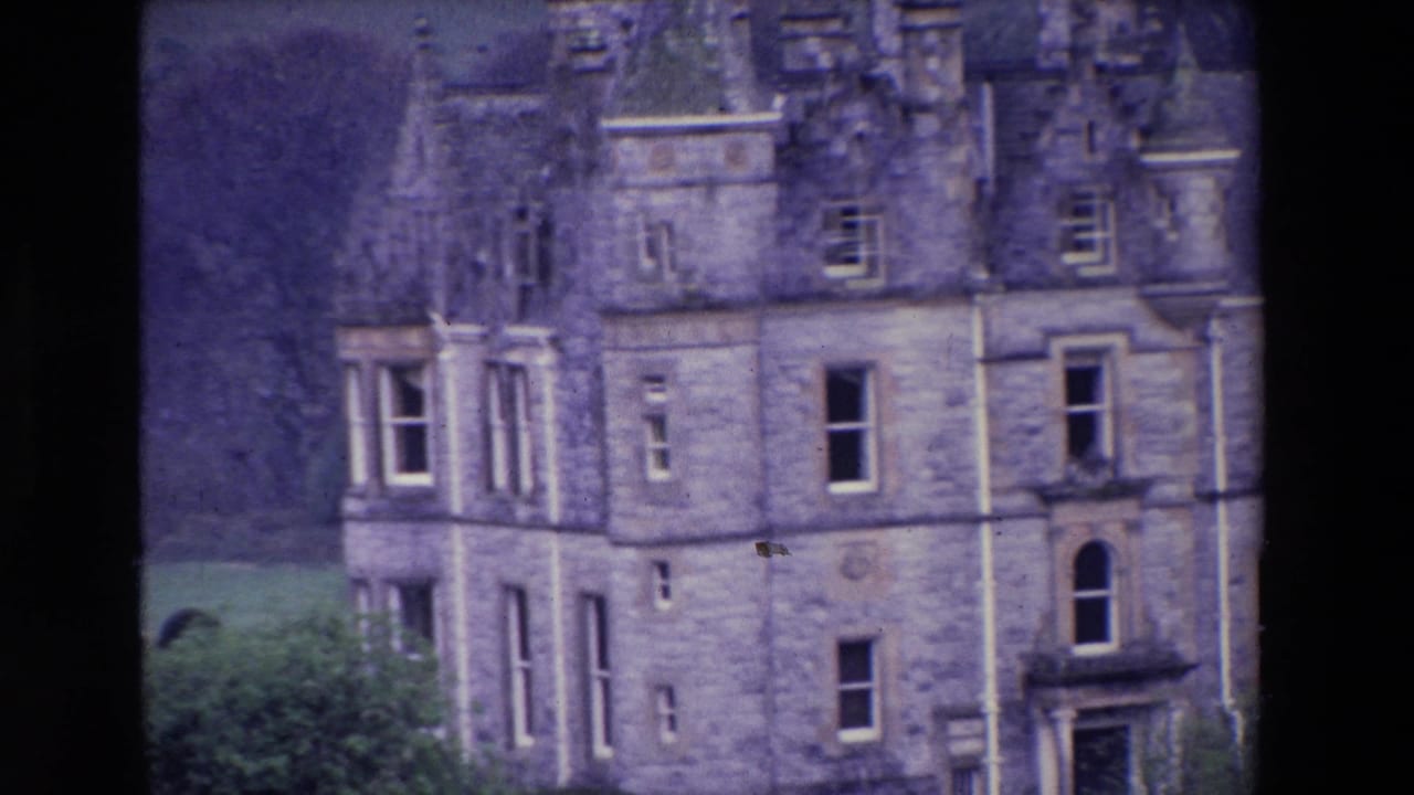 Closer 1969 Ireland home-movie view of a stone castle facade, showing a turreted corner, tall windows, dormers, roof details, and grass below.