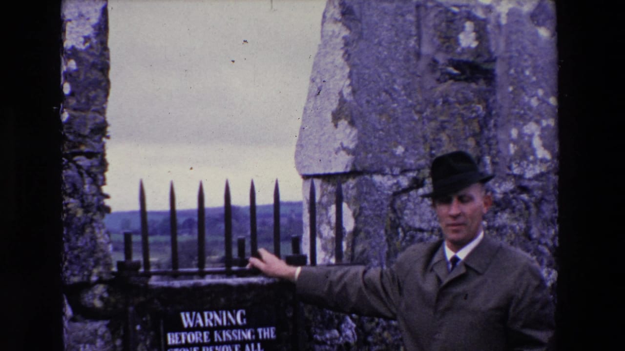 The man remains posed at the stone ruin in Ireland, extending one arm toward the iron gate and the partially visible warning sign below it.