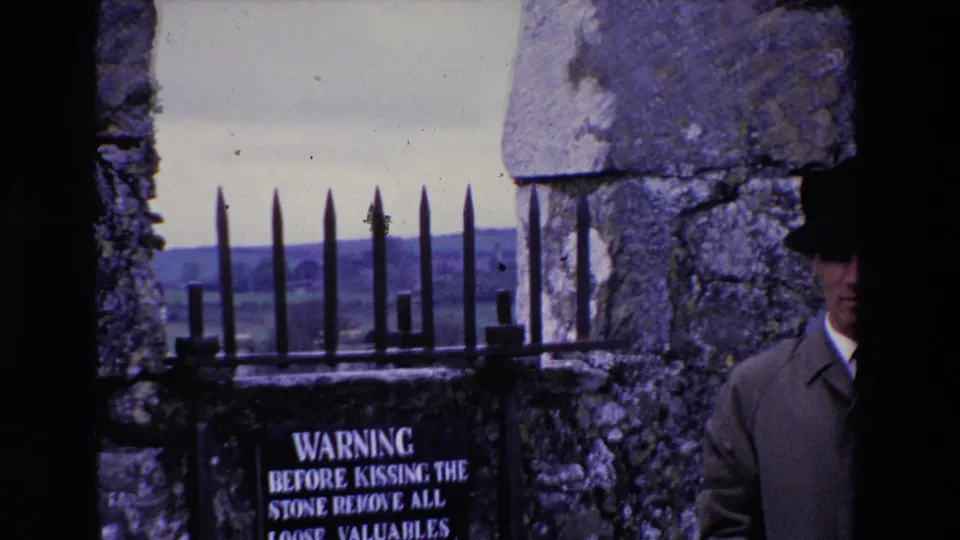 The frame centers on the iron spikes and warning sign at the stone wall, with the man's hat and partly obscured face entering from the right edge.