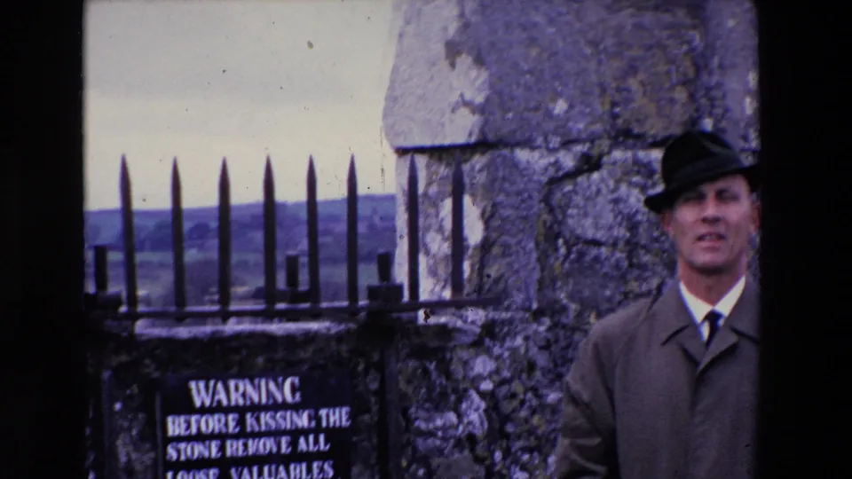 At the end of the 1969 Ireland clip, the man stands near the right edge while the warning sign, iron gate, weathered stonework, and rural view remain visible.