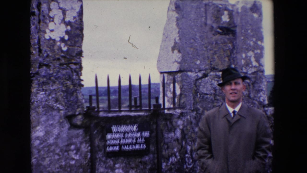 In 1969 Ireland, a man in a dark coat and brimmed hat poses near weathered stone walls, a black iron gate, and a sign warning visitors before kissing the stone.