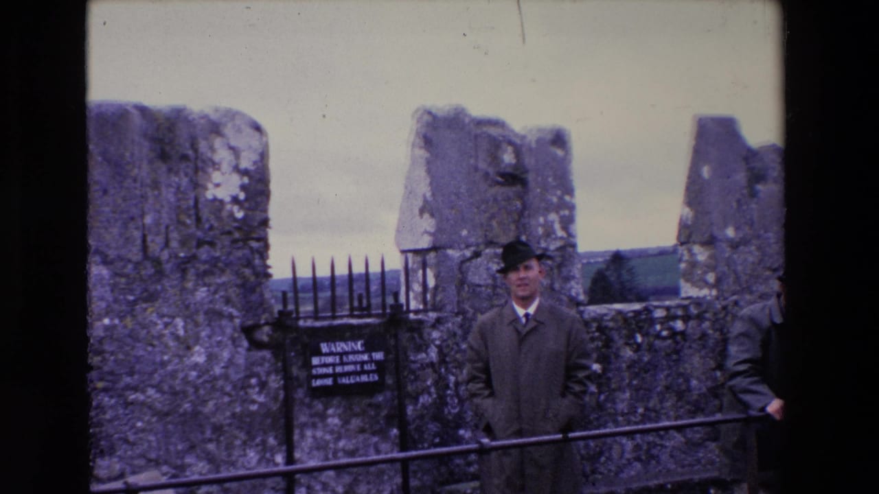 In 1969 Ireland, the tourist remains framed against Blarney Castle ruins, with the warning sign, spiked gate, and handrail visible in the foreground.