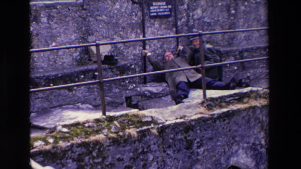 A man reclines on the ledge while another man sits beside him behind the railing.