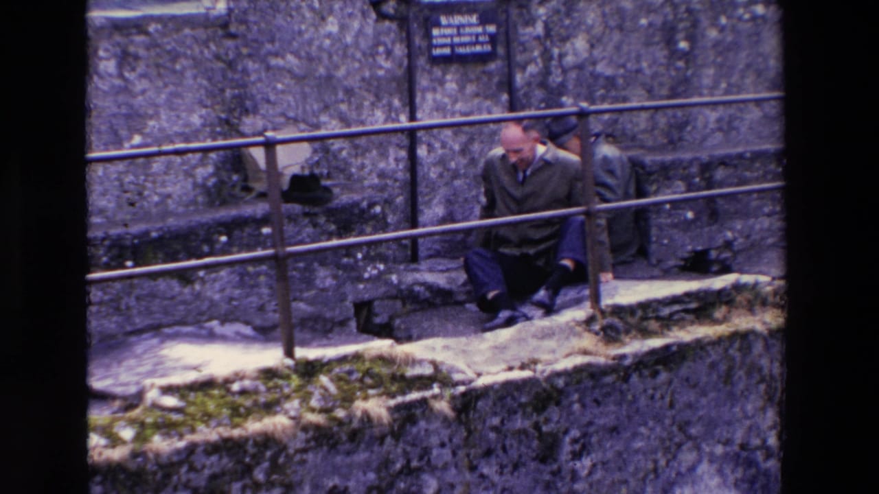 Man sits or scoots near a railing on stone steps in front of rough castle masonry.