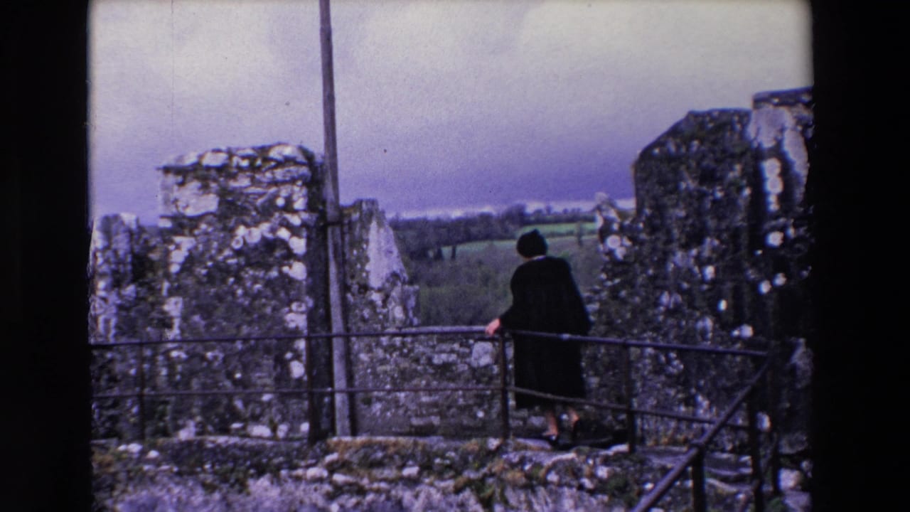 Woman stands near a railing between ruined stone walls with countryside behind her.