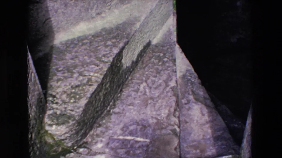 The final 1969 Ireland frame emphasizes the texture of stone paving, weathered walls, and a dark recess within the ruins, with part of the visitor still at the right edge.