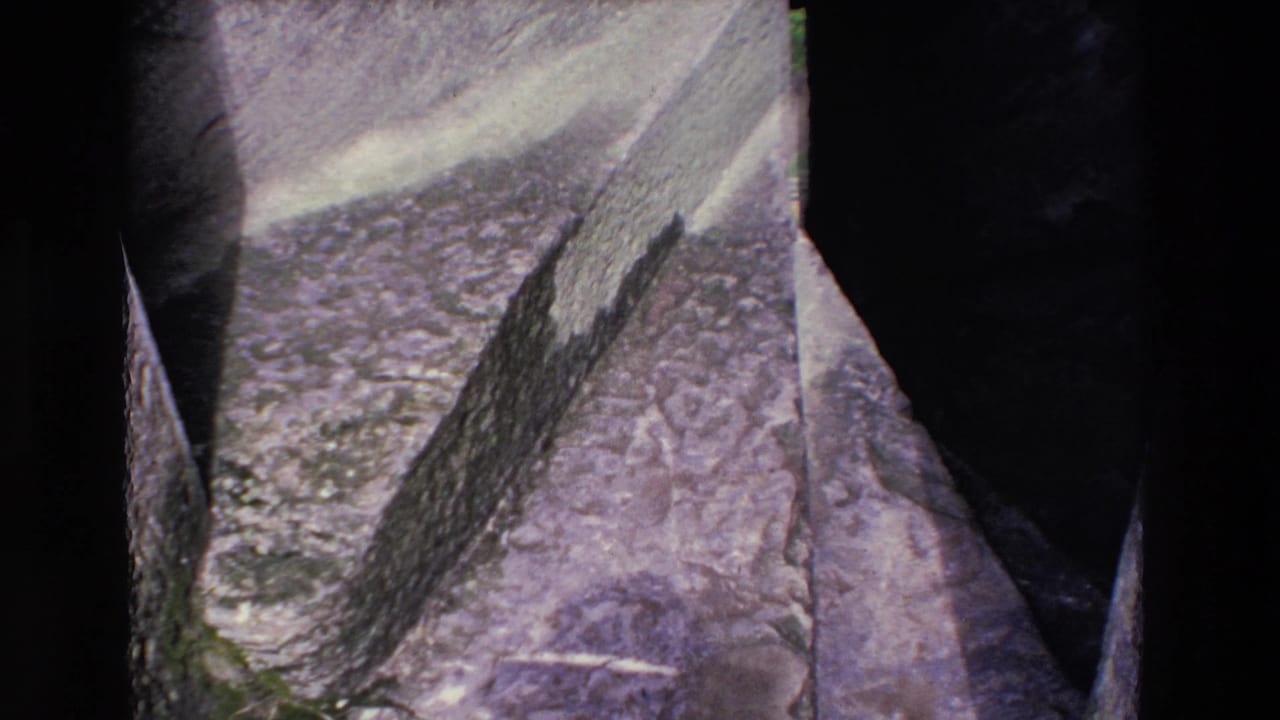 1969 Ireland 8mm frame looking down over weathered rock on a steep mountain slope, with dark gaps, rough stone texture, and aged purple-gray color shift.