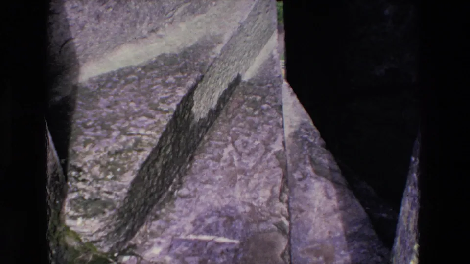 1969 Ireland 8mm frame holding on the textured surface of a rugged mountain slope, with muted color, shadowed rock gaps, and slight handheld framing.