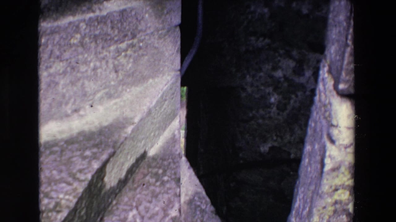 1969 Ireland 8mm frame showing rough, weathered stone masonry and a shadowed gap or passage edge in a historic structure.
