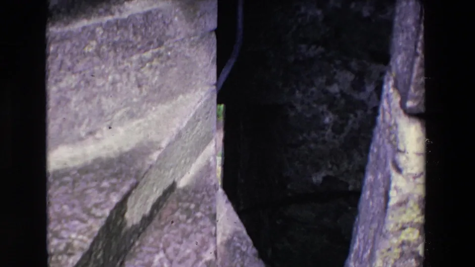 1969 Ireland 8mm frame showing rough, weathered stone masonry and a shadowed gap or passage edge in a historic structure.
