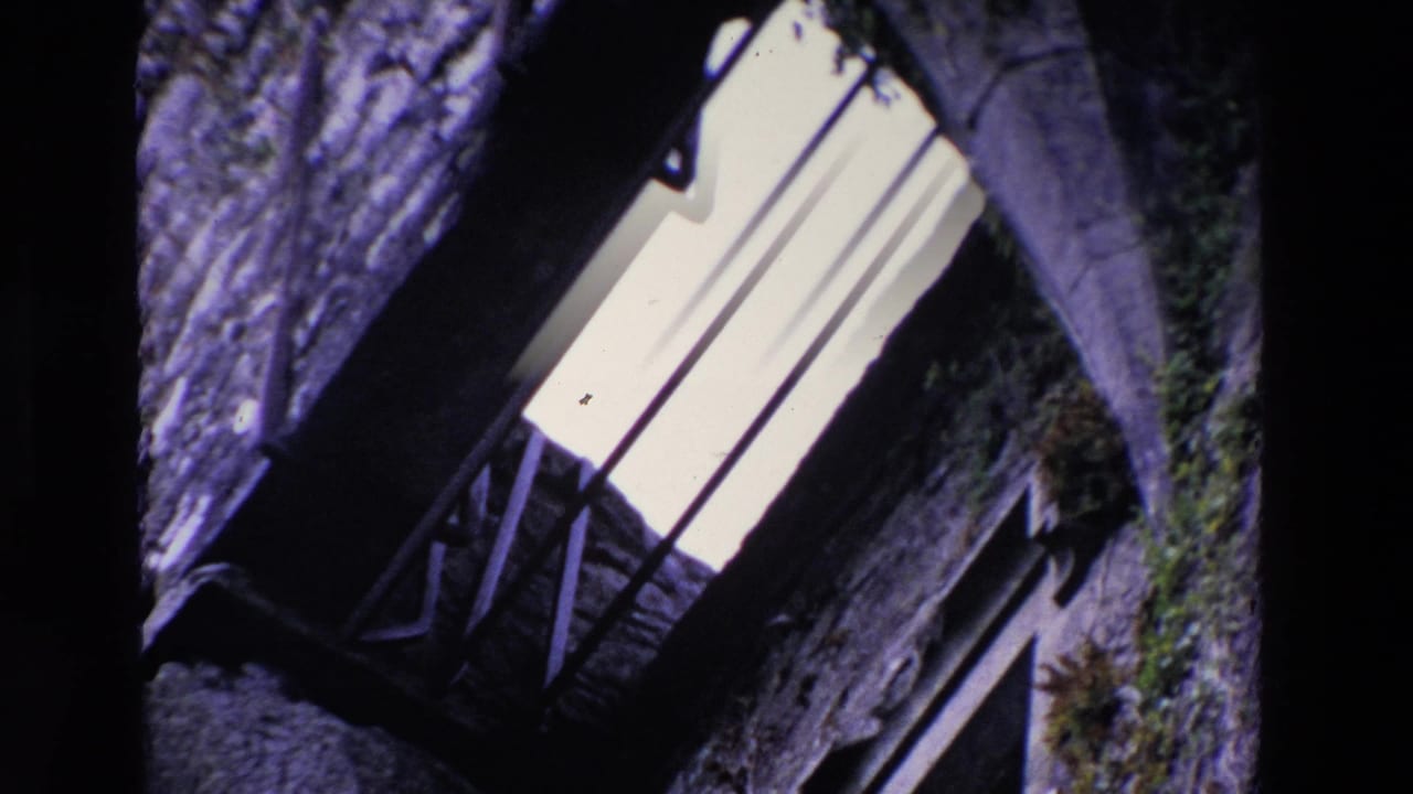 1969 Ireland 8mm frame showing a tilted close view of weathered stonework, a bright barred window, and shadowed architectural recesses.