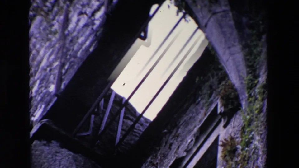 1969 Ireland 8mm frame showing a tilted close view of weathered stonework, a bright barred window, and shadowed architectural recesses.