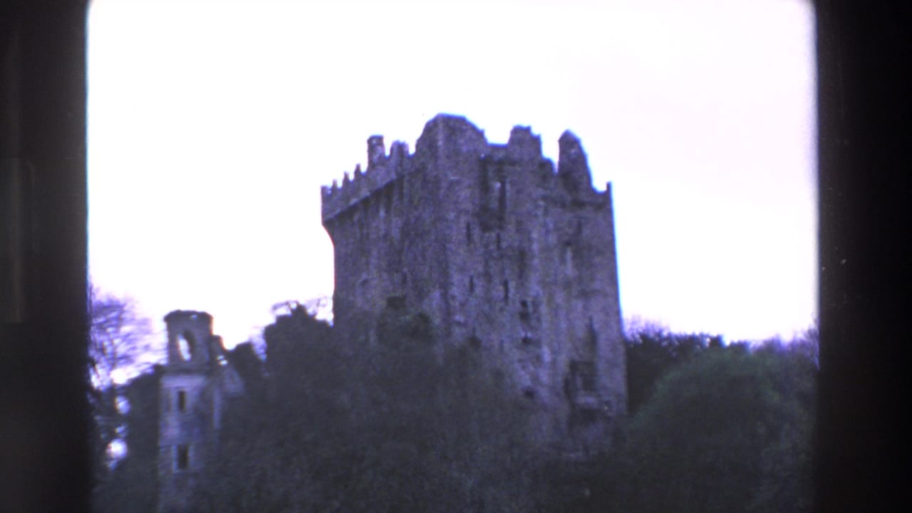 1969 Ireland 8mm frame showing a crenellated stone castle tower with a smaller ruin nearby, partly obscured by trees and dark frame edges.