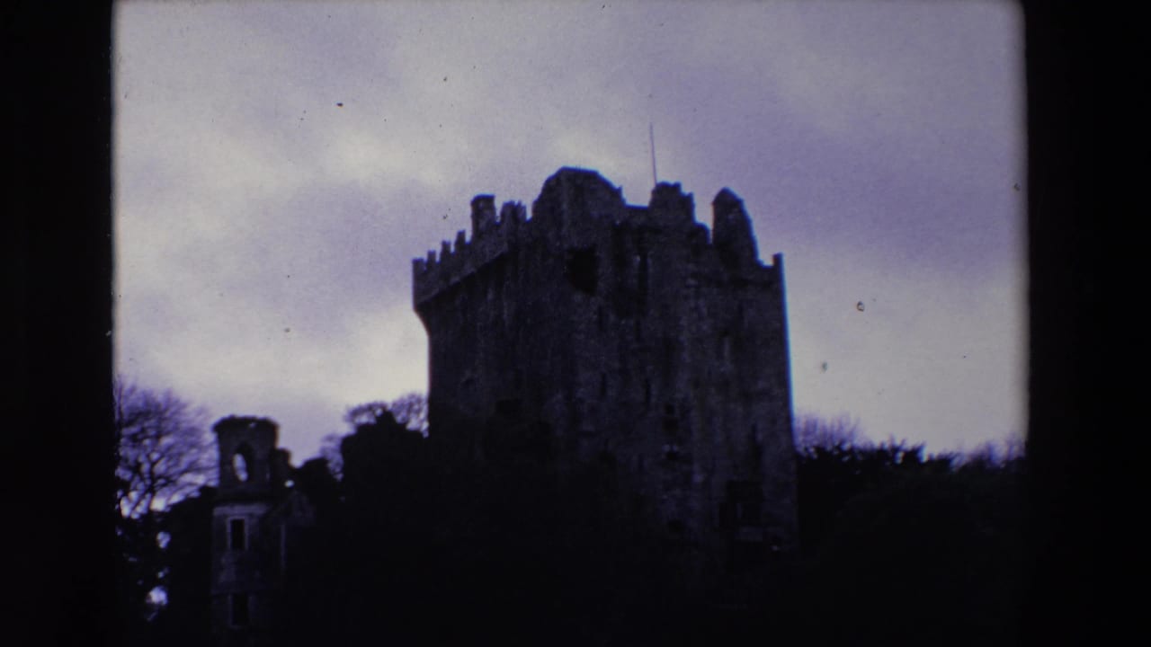 1969 Ireland 8mm frame with the castle tower darker in silhouette, its battlements rising above trees beneath an overcast sky.