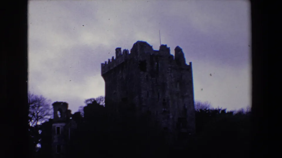1969 Ireland 8mm frame with the castle tower darker in silhouette, its battlements rising above trees beneath an overcast sky.