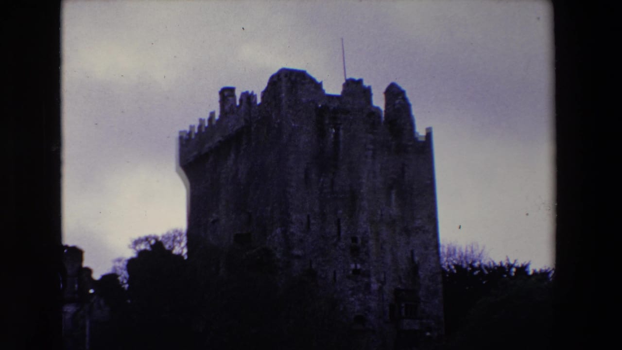 1969 Ireland 8mm frame showing a dark, weathered stone castle with crenellated towers silhouetted against a pale overcast sky.
