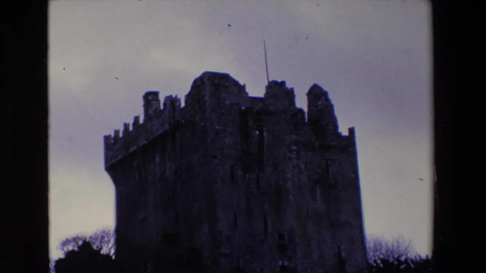 1969 Ireland 8mm frame with the castle upper walls, broken tower profiles, and dark stone mass framed by overcast sky.