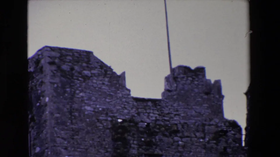 1969 Ireland frame with a close view of weathered castle-like stonework, dark scan borders, and a vertical line crossing the pale sky.