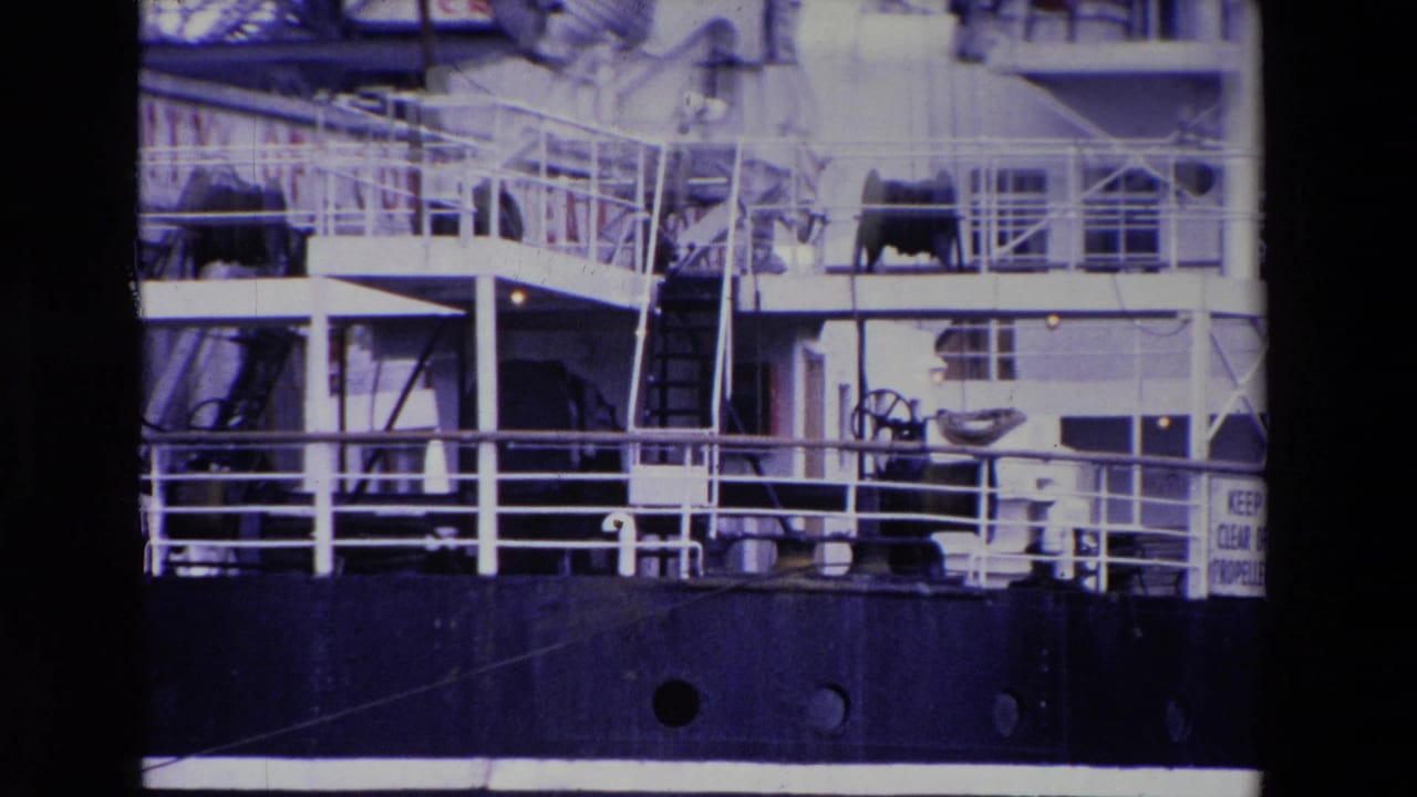 Midsection of the docked INNISFALLEN in Ireland, with white railings, deck structures, lifeboat gear, and portholes visible on the dark hull.