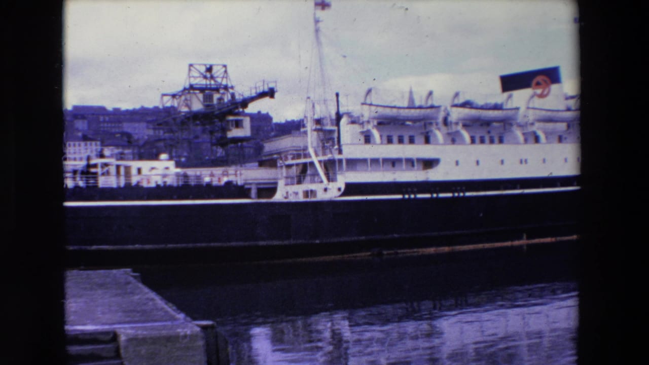 1969 Ireland 8mm frame of a stationary white passenger ship with lifeboats and rigging, seen from a dock with harbor cranes in the background.