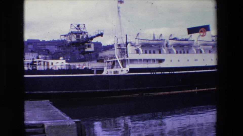 1969 Ireland 8mm frame of a stationary white passenger ship with lifeboats and rigging, seen from a dock with harbor cranes in the background.