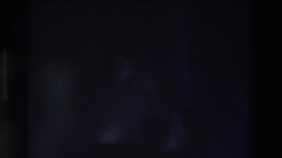 Dark, grainy 8mm frame from the clip with no clearly identifiable person or object visible.