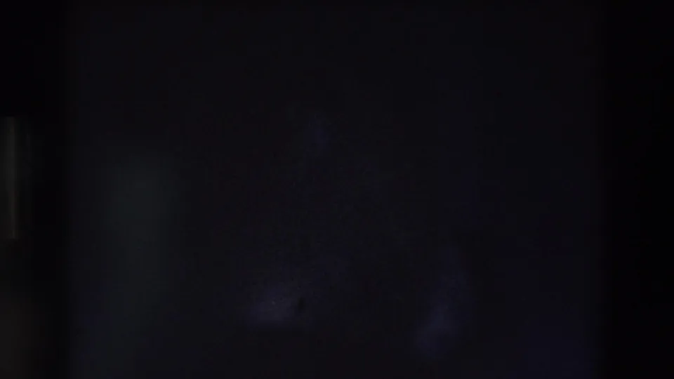 A very dim 8mm frame with shadowed shapes and little identifiable detail before the exterior flag shot.