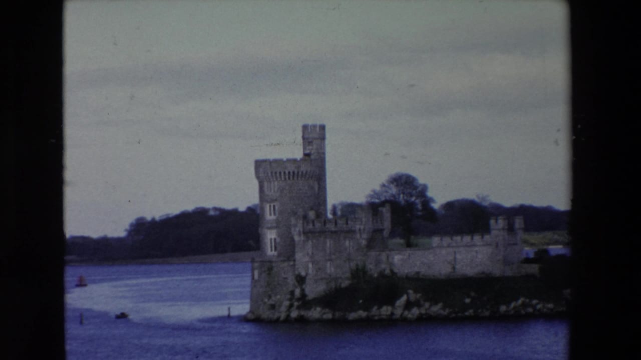 1969 Ireland 8mm frame showing a stone castle with battlements and a tall tower on a rocky river edge, seen from across the water.