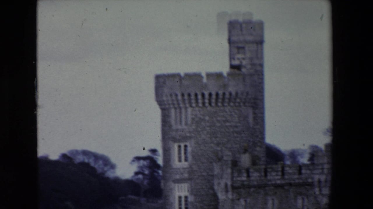 1969 Ireland 8mm frame showing a soft-focused crenellated stone castle tower beside calm water and dark trees in the background.