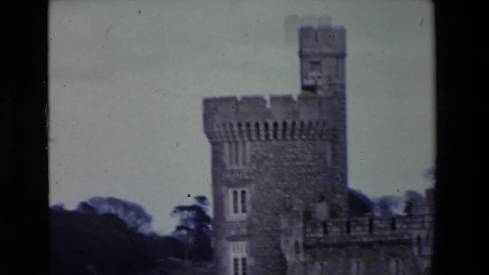 1969 Ireland 8mm frame showing a soft-focused crenellated stone castle tower beside calm water and dark trees in the background.