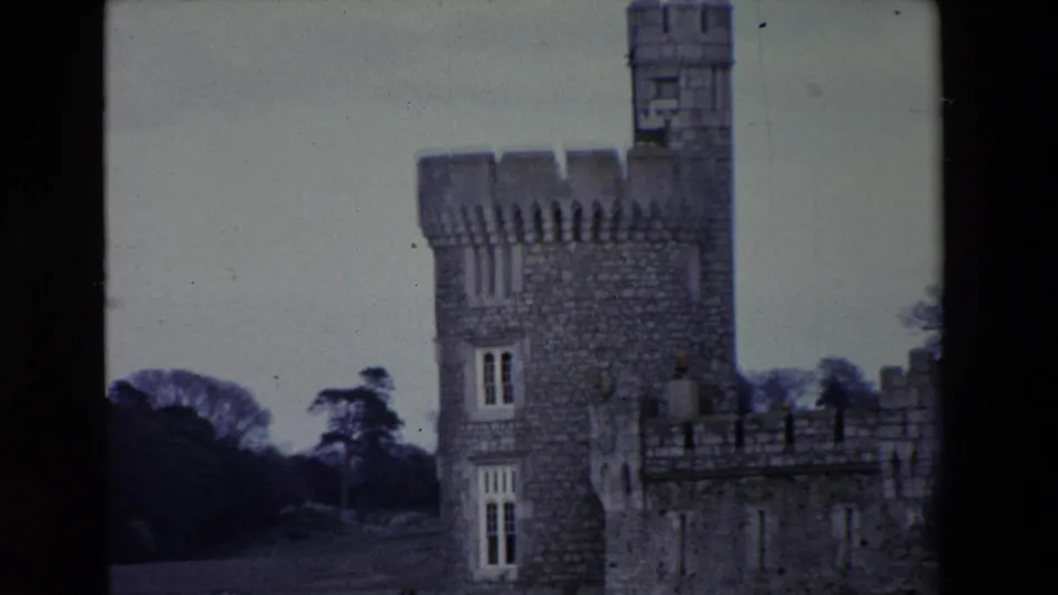 1969 Ireland home-movie frame showing the castle tower more centered, with crenellated parapets, tall windows, riverside grounds, and trees beyond.