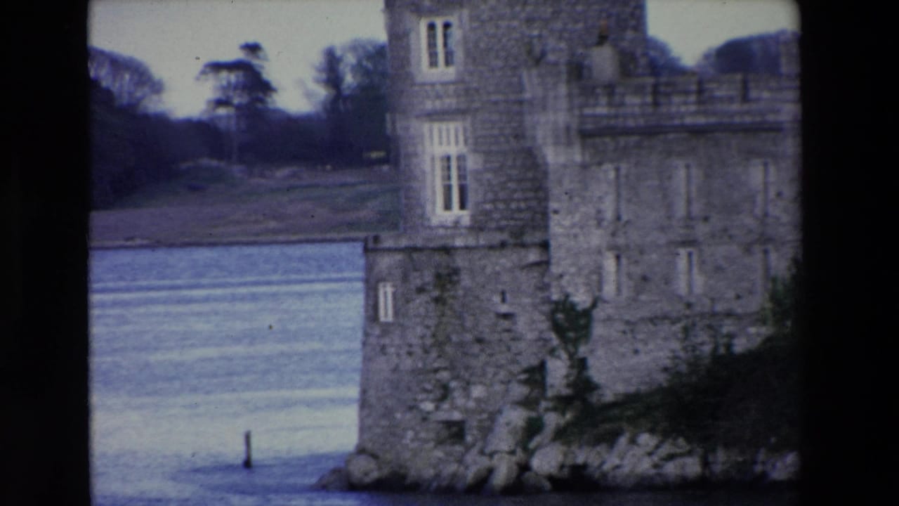 1969 Irish home-movie frame showing part of a stone castle beside calm water, with narrow windows, rough masonry, and open grounds beyond.