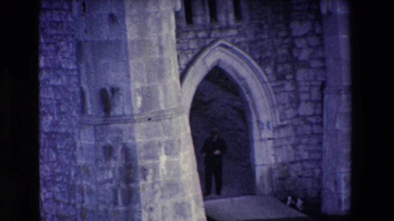 Man standing farther back in a stone archway under dim blue-toned light.